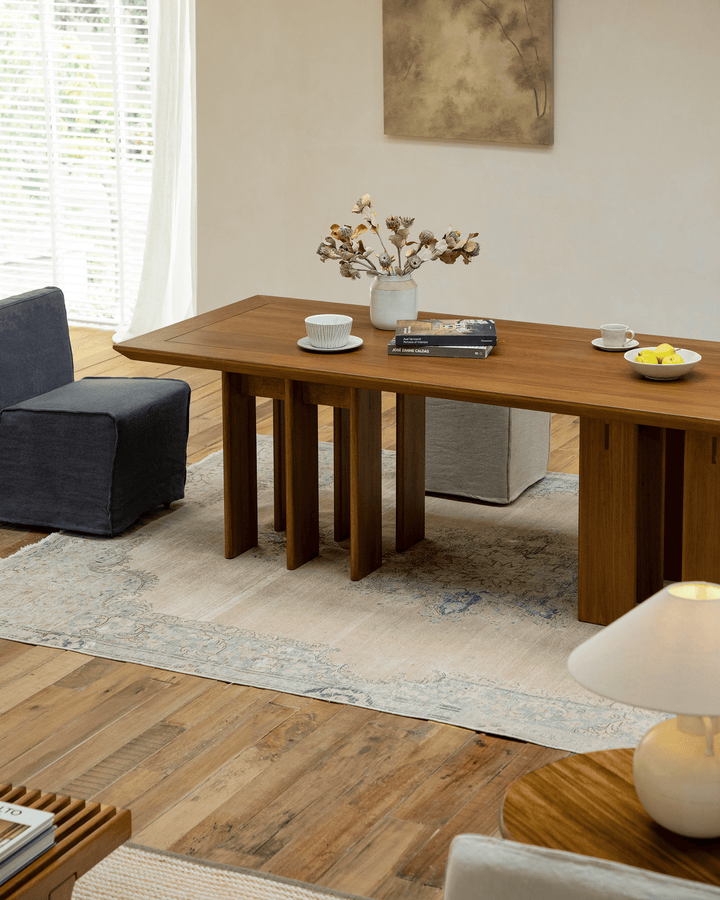 Elegant teak dining table with multi-leg design, decorated with a vase and fruits.