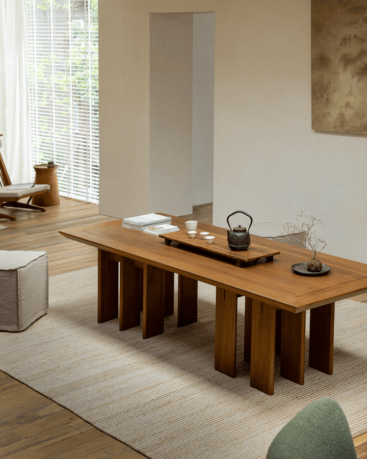 Elegant teak dining table with multi-leg design, tea set, and light-filled interior.
