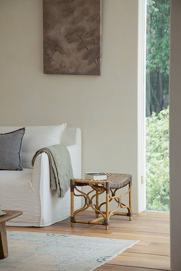 Handcrafted Melange Stool in Manau rattan next to a white sofa in a bright room.