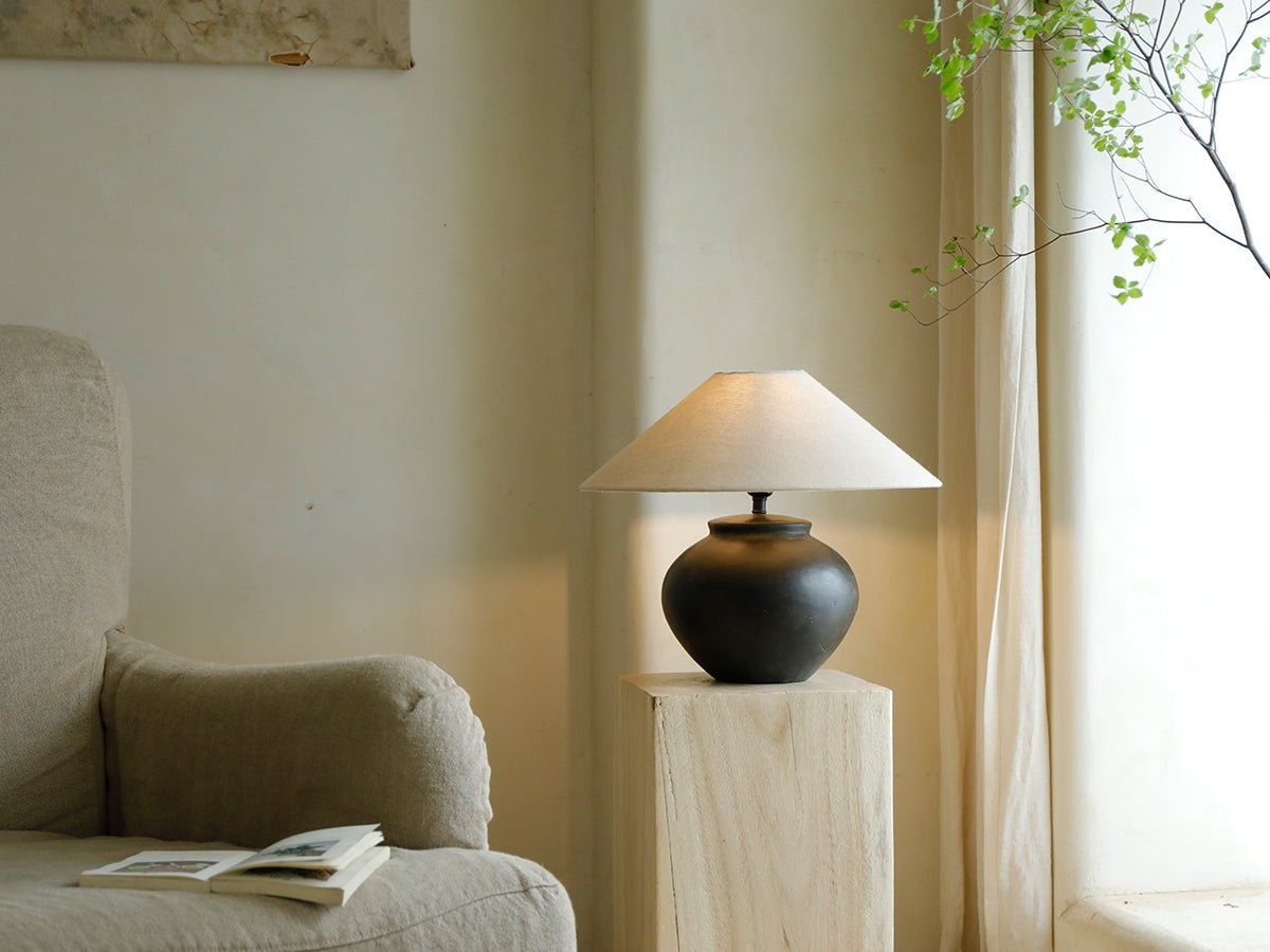 Clay moon lamp with beige lampshade, dark base on wooden stand, and armchair.