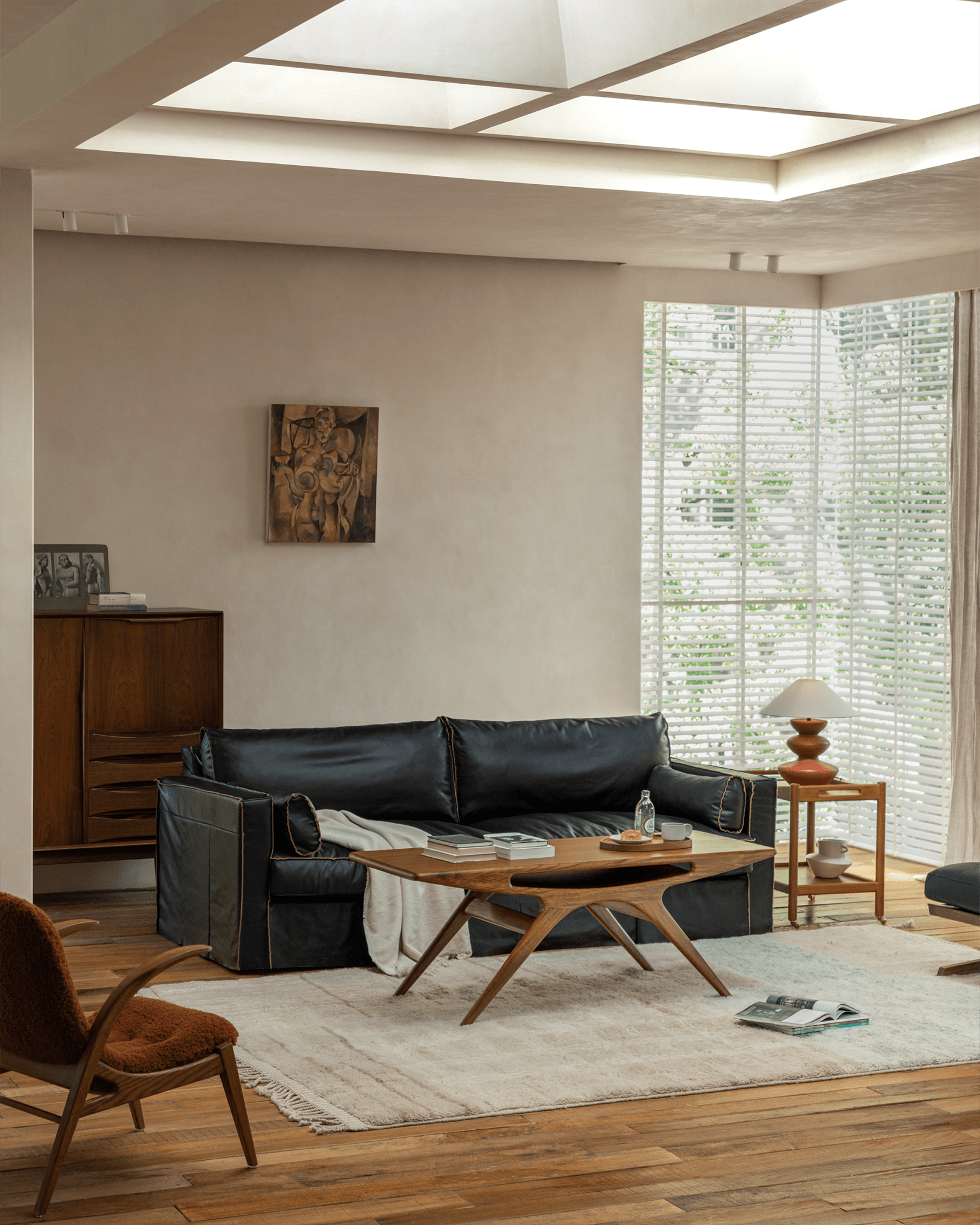 Simile Teak Coffee Table in a modern living room setting with black sofa, showing smile cutout and angled legs