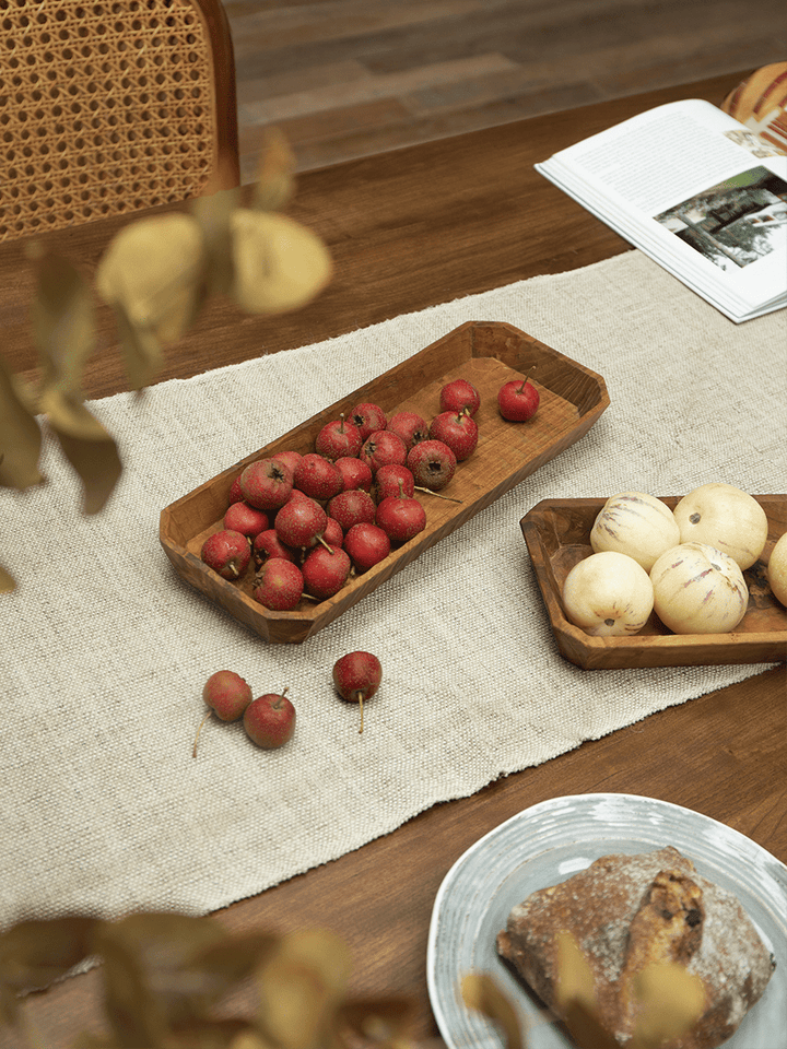 Handcrafted teak wood serving trays with fruit on a rustic wooden table.