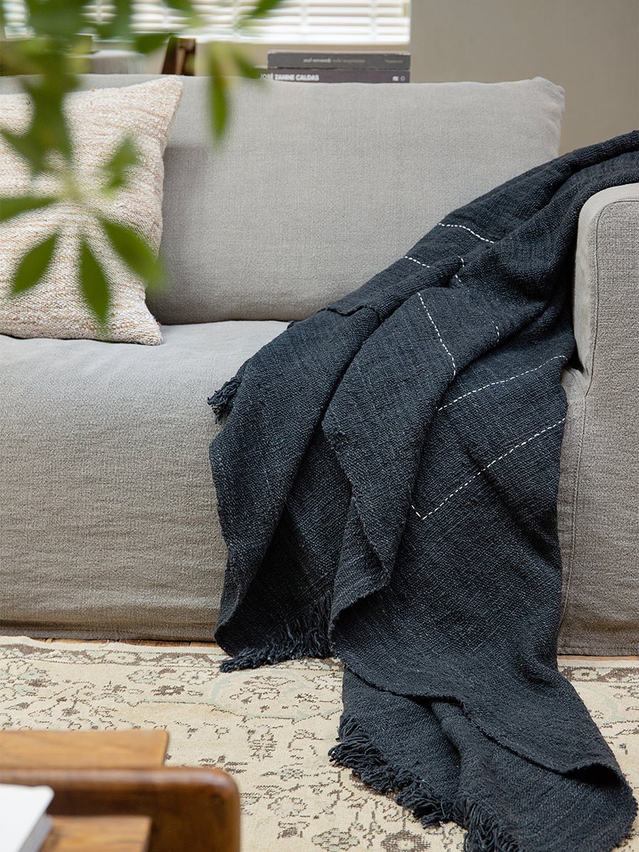 Dark gray cotton blanket on a sofa with white stitching; Cotton Blanket