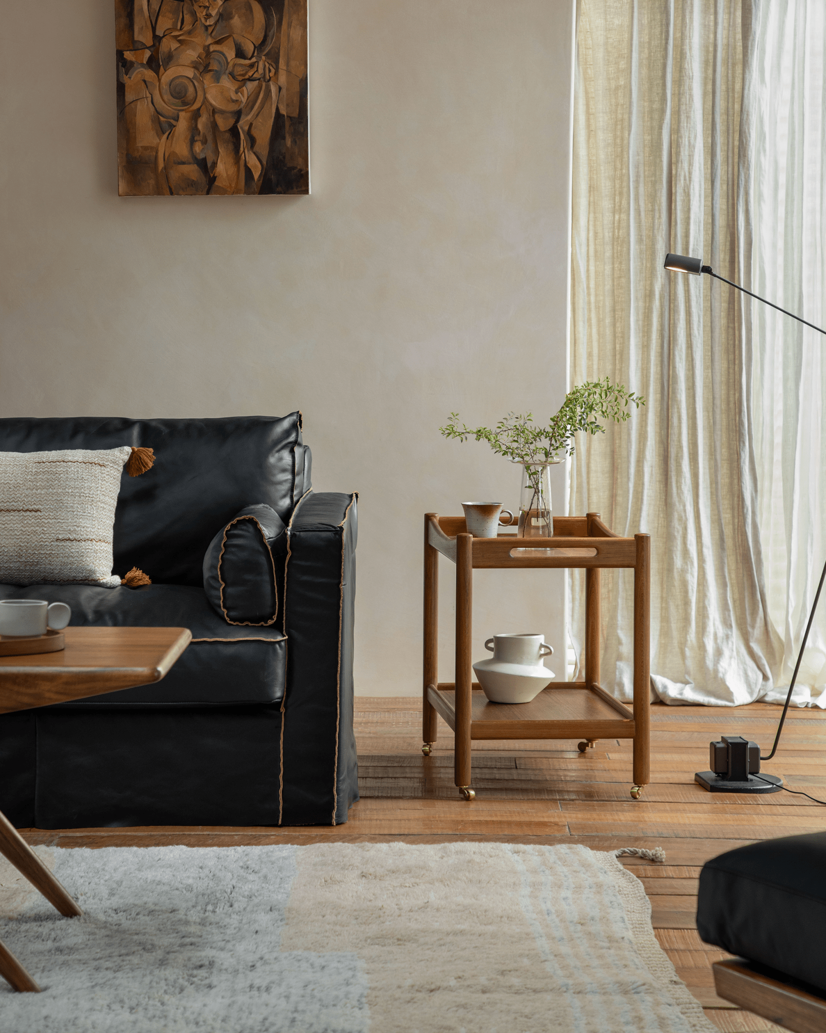 Brooklyn Bar Cart styled in living room setting, wooden cart with double-layer, brass casters, handle, and black leather sofa