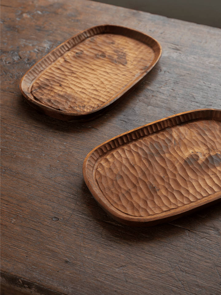 Handcrafted teak wood serving trays with unique ripple texture on wooden table.