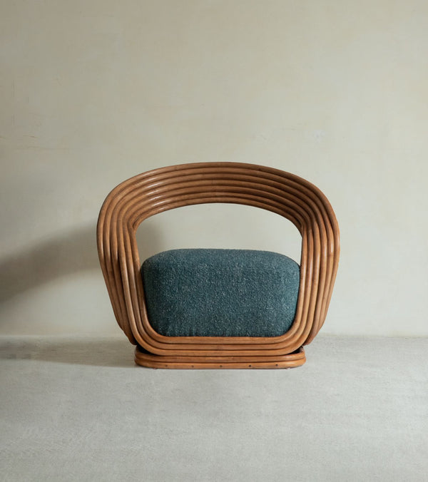 The Undina Rattan Lounge Chair by ZM Home features a curved wooden frame and textured green upholstery, set against a plain beige wall on a light carpeted floor.