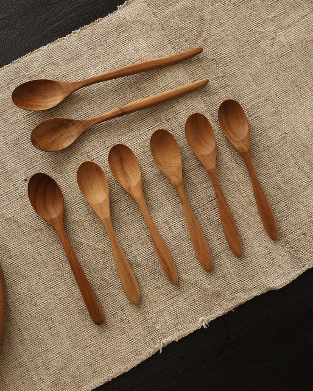 Set of wooden table spoons, natural wood finish, placed on a beige linen fabric, product shot.
