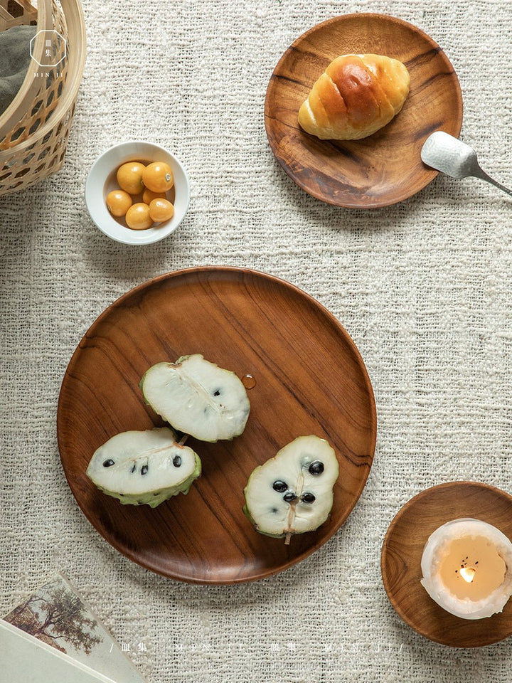 Handcrafted teak wood plates with fruit slices and a croissant on textured fabric.