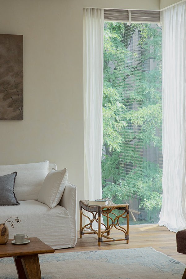 Melange Stool in Manau rattan next to white sofa and window with greenery view.