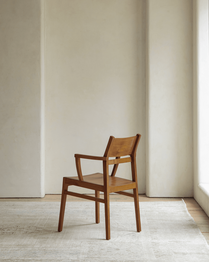Minimalist wooden Hug Chair in natural finish against a plain wall.