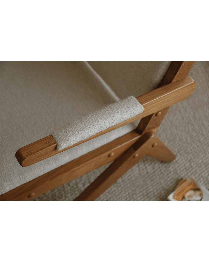 Close-up of Scissors Chair armrest with gray upholstery and wooden frame.