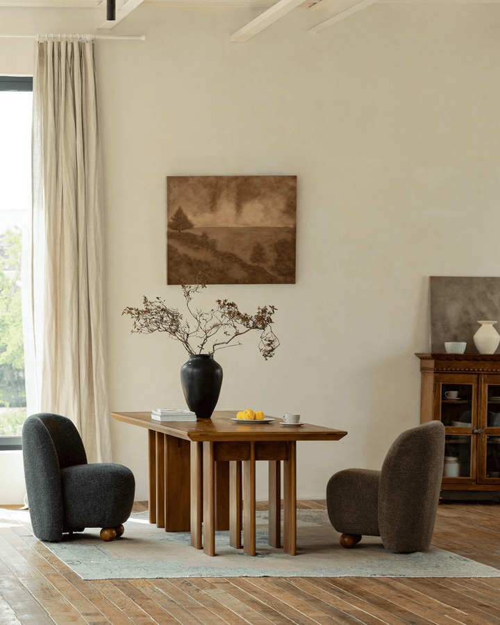 Modern wooden dining table with black vase and armchairs in a bright interior
