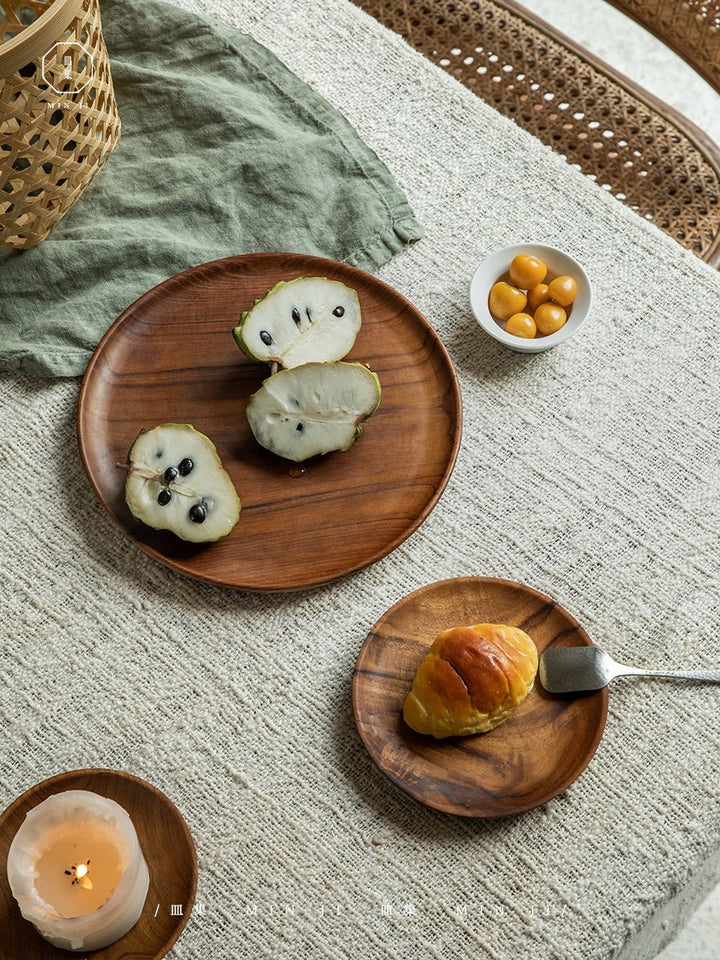 Teak wood plates with fruit slices and a croissant on textured fabric