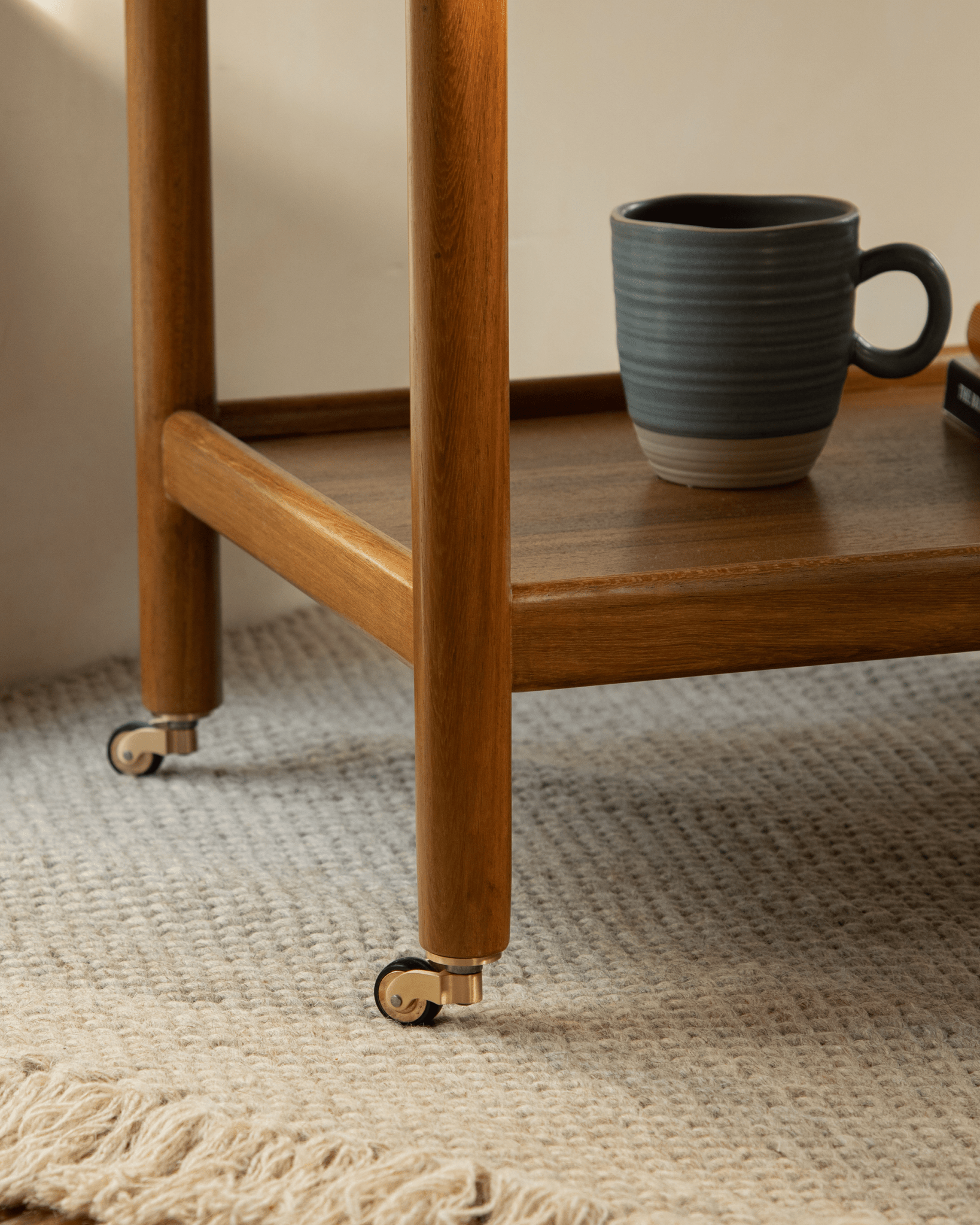 Brooklyn Bar Cart detail: Wooden bar cart with brass caster, a cup, and a rug. Stylish mobile storage.