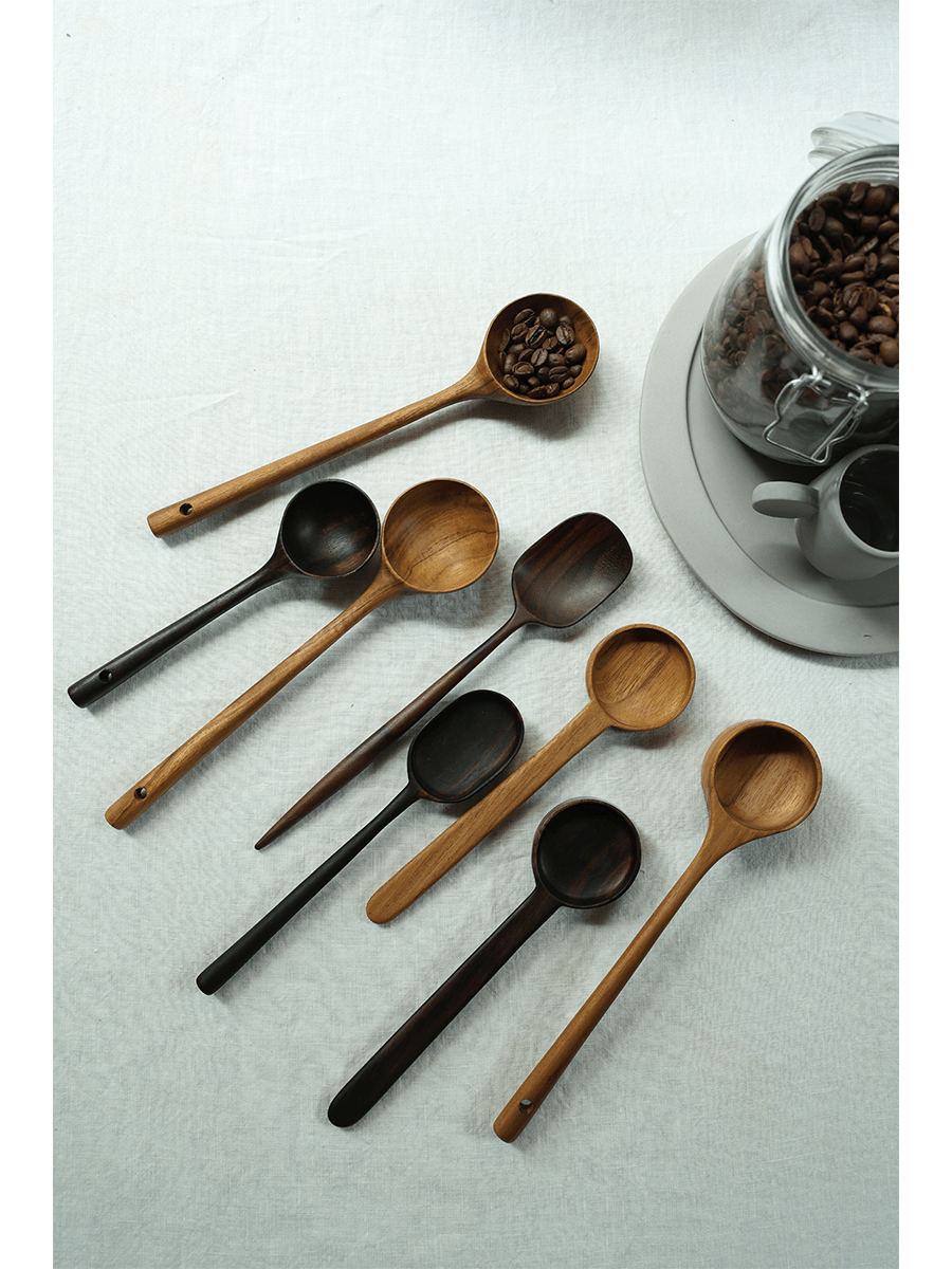 Teak coffee spoons in varying shades of brown and black on a white linen surface, with coffee beans.