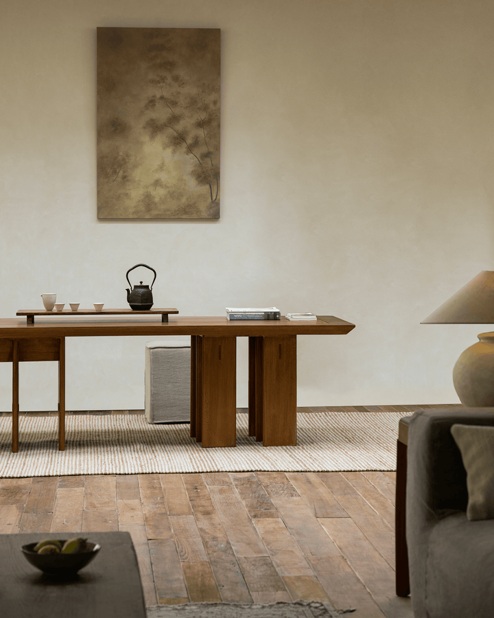 Minimalist teak dining table with a tea set and artistic decor in a bright interior.