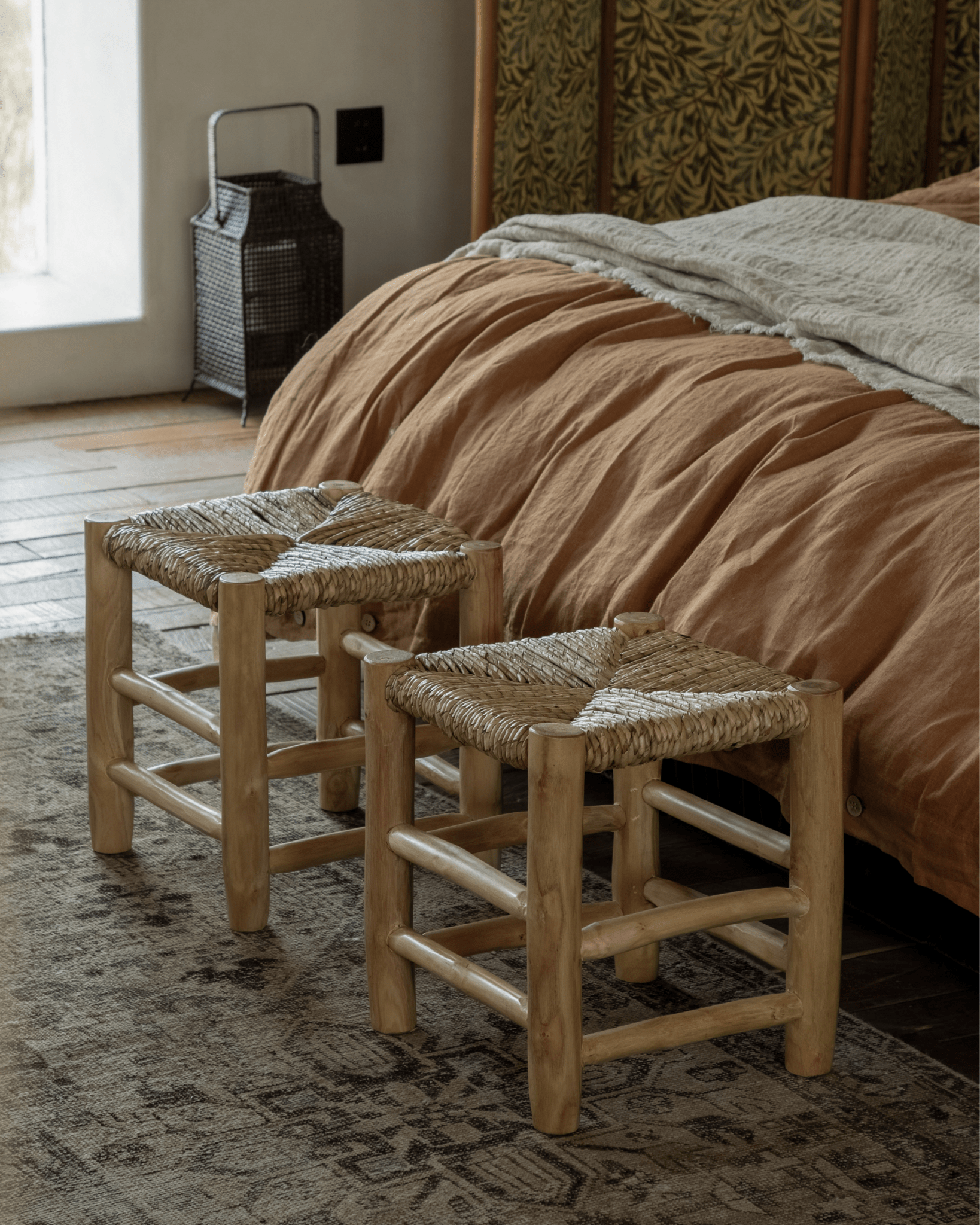 Isla Handwoven Stool set in a bedroom. Natural wood frame, woven seat, and earthy tones.