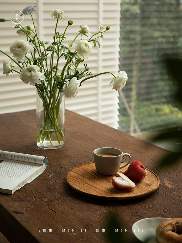 Cozy dining scene with coffee, fruit, and vase of white flowers on a wooden table.