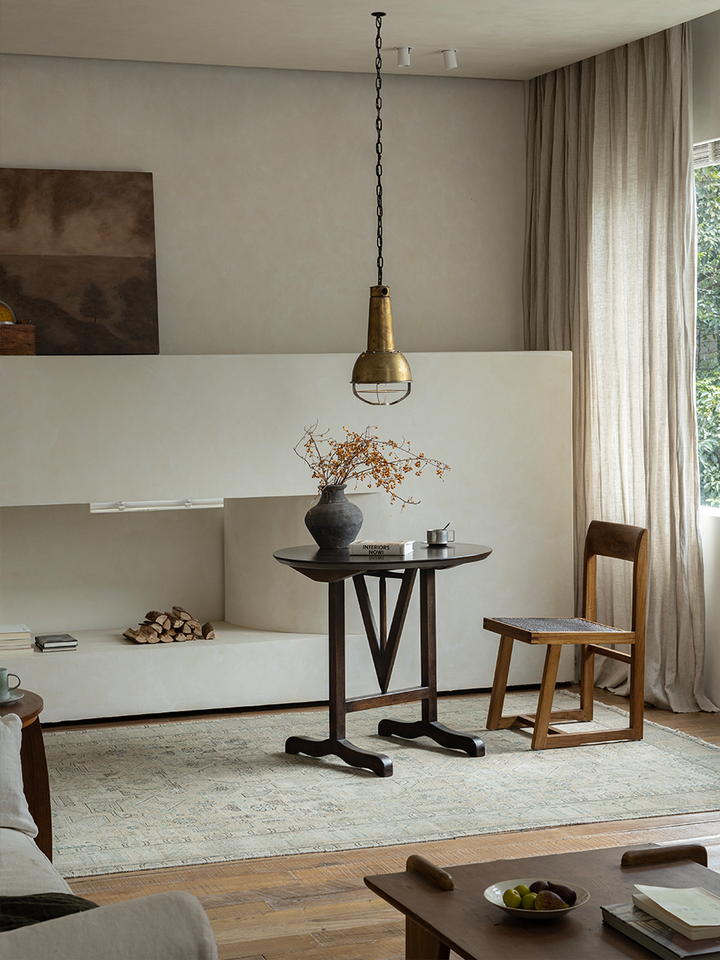 V-Leg round table in a cozy living room with dark wood finish and decorative elements.