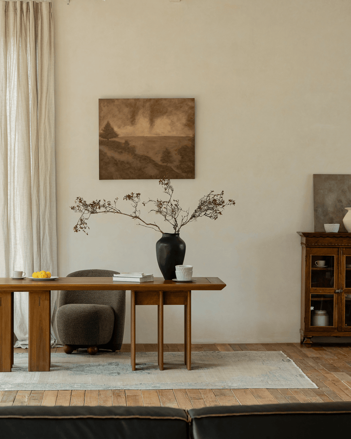 Elegant teak dining table with vase and flowers, soft armchair in a bright interior.