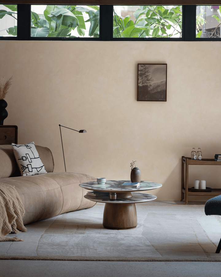 Stylish round marble side table with wooden base, cup, and decor in modern living room.