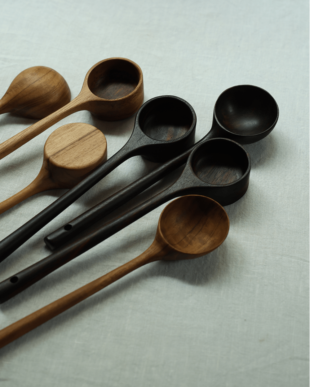Teak coffee spoons, different shades of brown and black, elegant design on a linen surface.