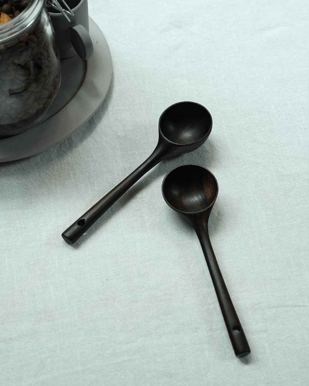 Teak coffee spoons, dark brown color, on white linen surface for coffee serving.
