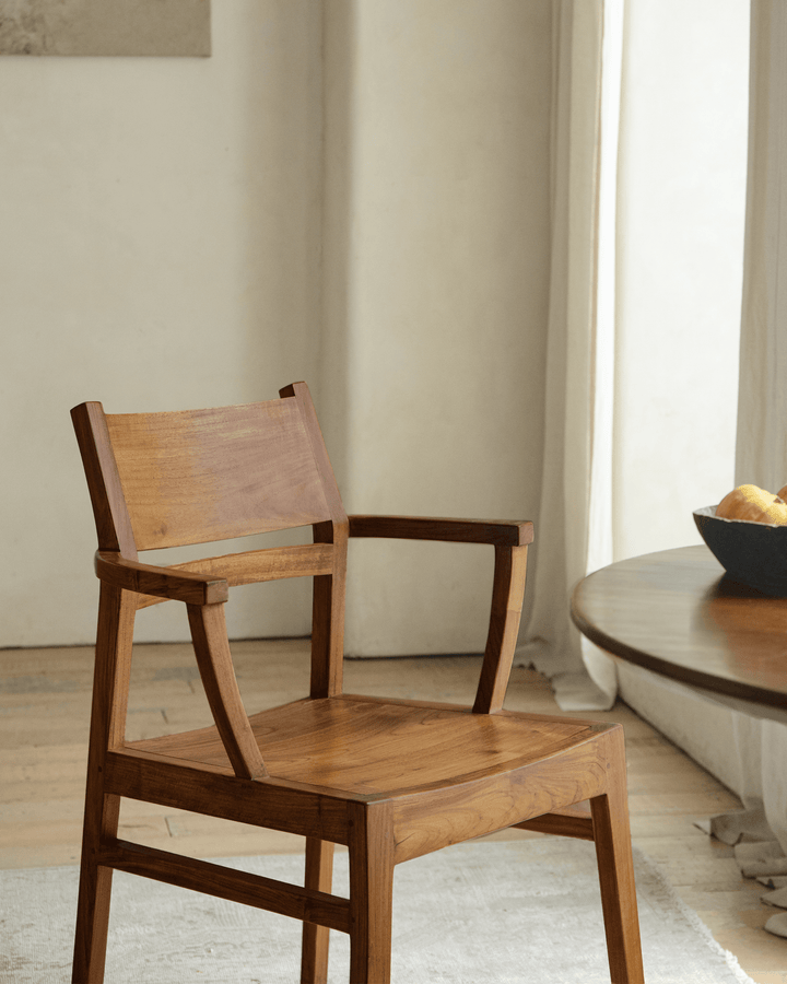 Minimalist wooden Hug Chair beside a round table with fruit bowl in a cozy dining area.