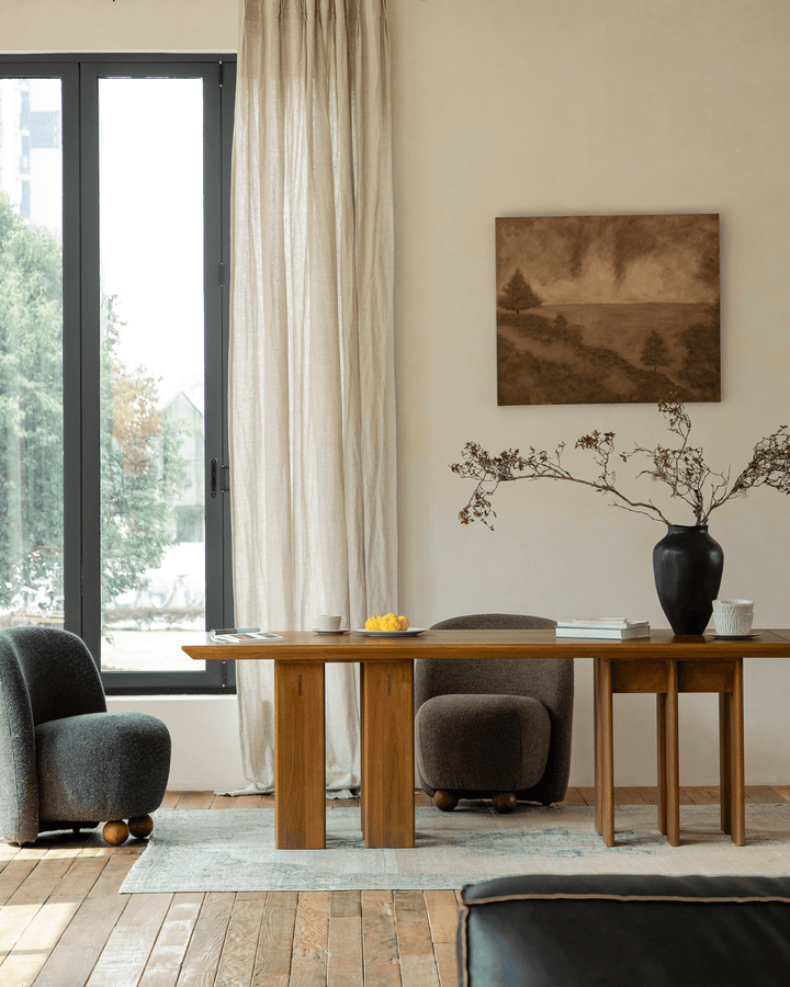 Elegant wooden dining table with two chairs, black vase, and fruit bowl in natural light.