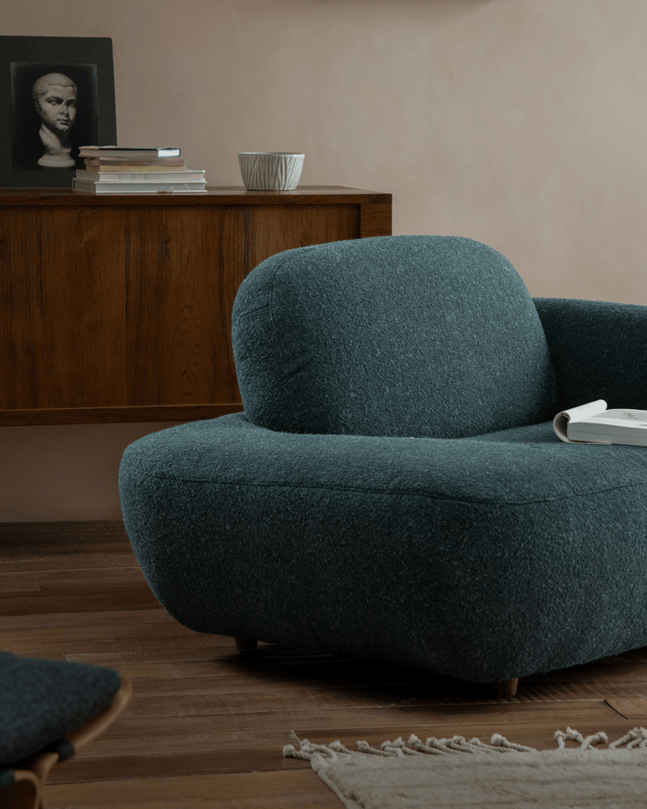Teal Gestein Bouclé Armchair in modern living room with wooden cabinet and decor.
