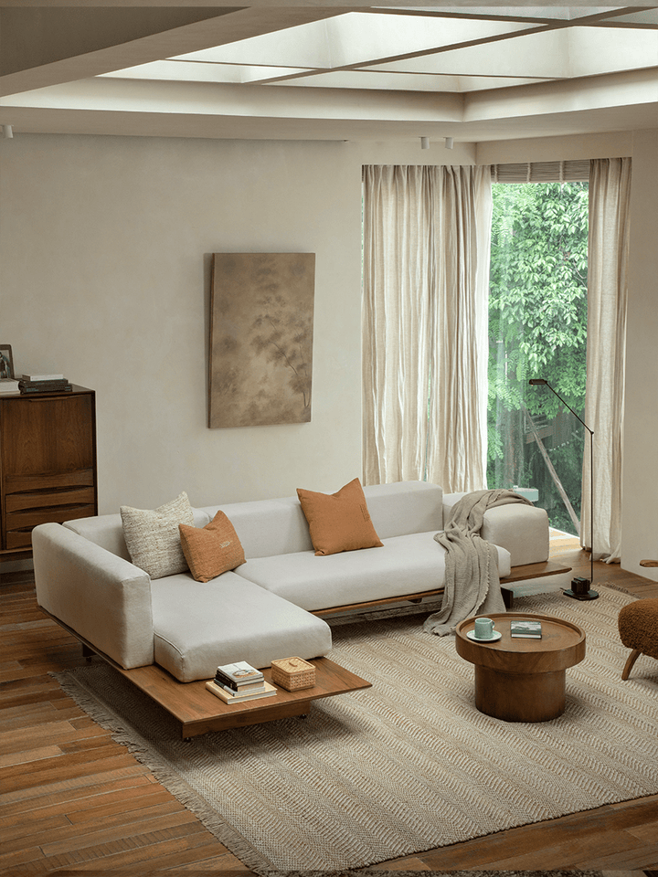 Modern linen modular sofa with teak base and orange cushions in minimalist living room.