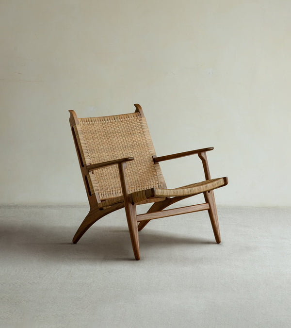 The Horn Lounge Chair by ZM Home, featuring an ergonomic design and woven rattan seat and backrest, sits on a light carpet against a plain beige wall, highlighting elegant handcrafted furniture.