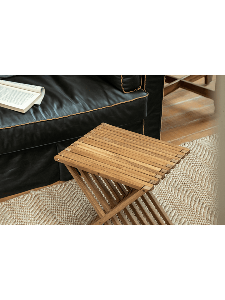 Teak wood folding coffee table beside a black sofa in a cozy living room.