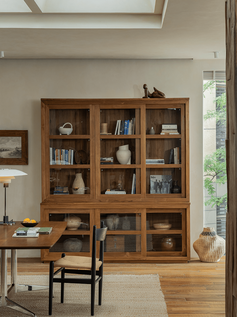 Teak wood glass front bookcase with sliding glass doors, displaying books and decor in a stylish living room setting.
