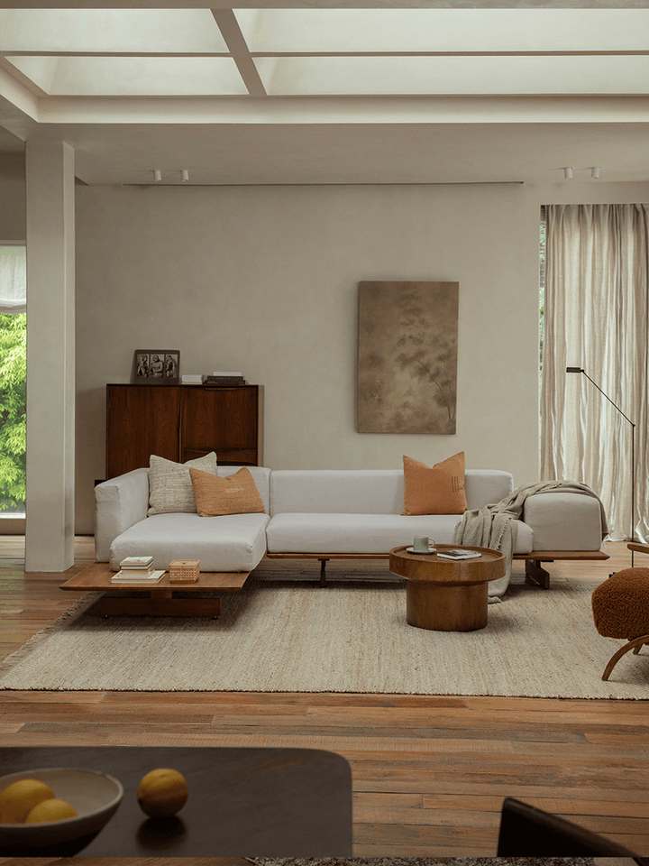 Linen modular sofa with orange cushions in a minimalist living room with wooden accents.