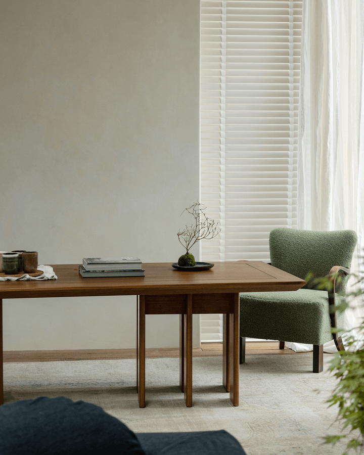 Minimalist teak dining table with decorative plant and green chair in bright interior.