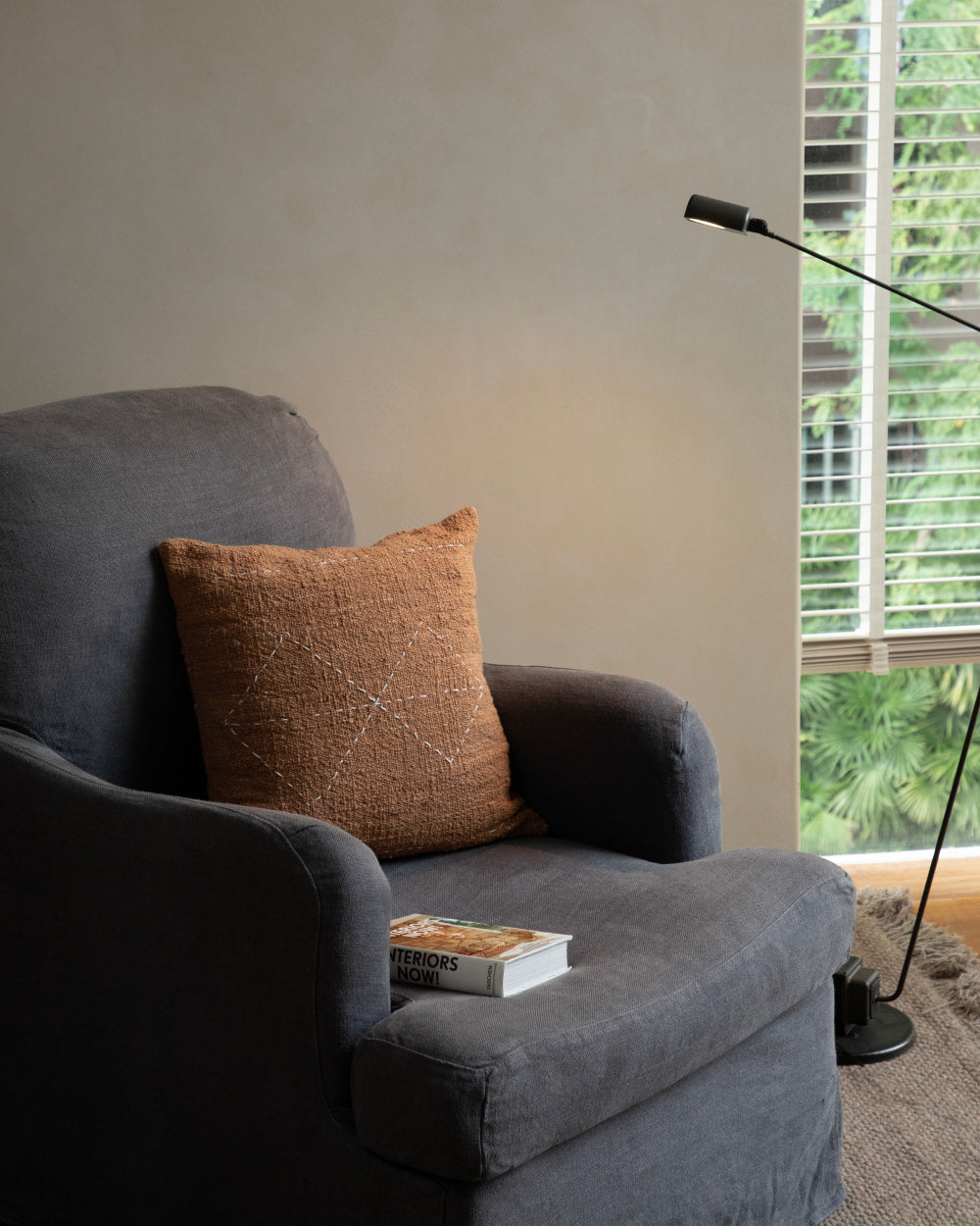 Handwoven Sylia Pillow in rust, featuring a subtle diamond stitch pattern on a grey armchair.