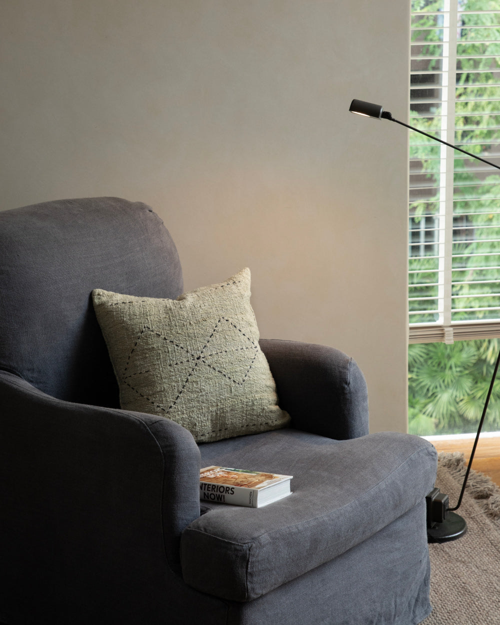 Sylia Pillow: Handwoven light green pillow with geometric stitching on a gray armchair, featuring "INTERIORS NOW!" book.
