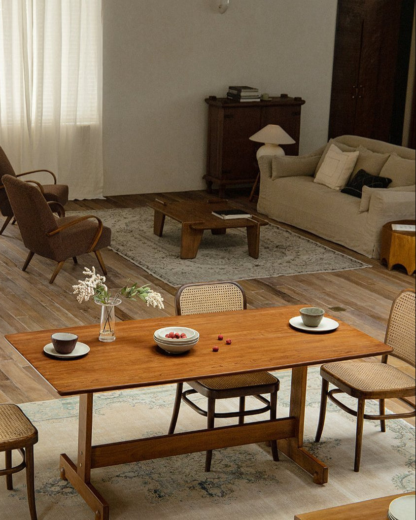 Hoof Dining Table with warm brown wood, I-shaped base, and woven chairs in a cozy dining setting.