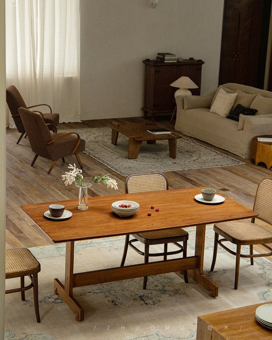 Hoof Dining Table with warm brown wood, I-shaped base, and woven chairs in a cozy dining setting.
