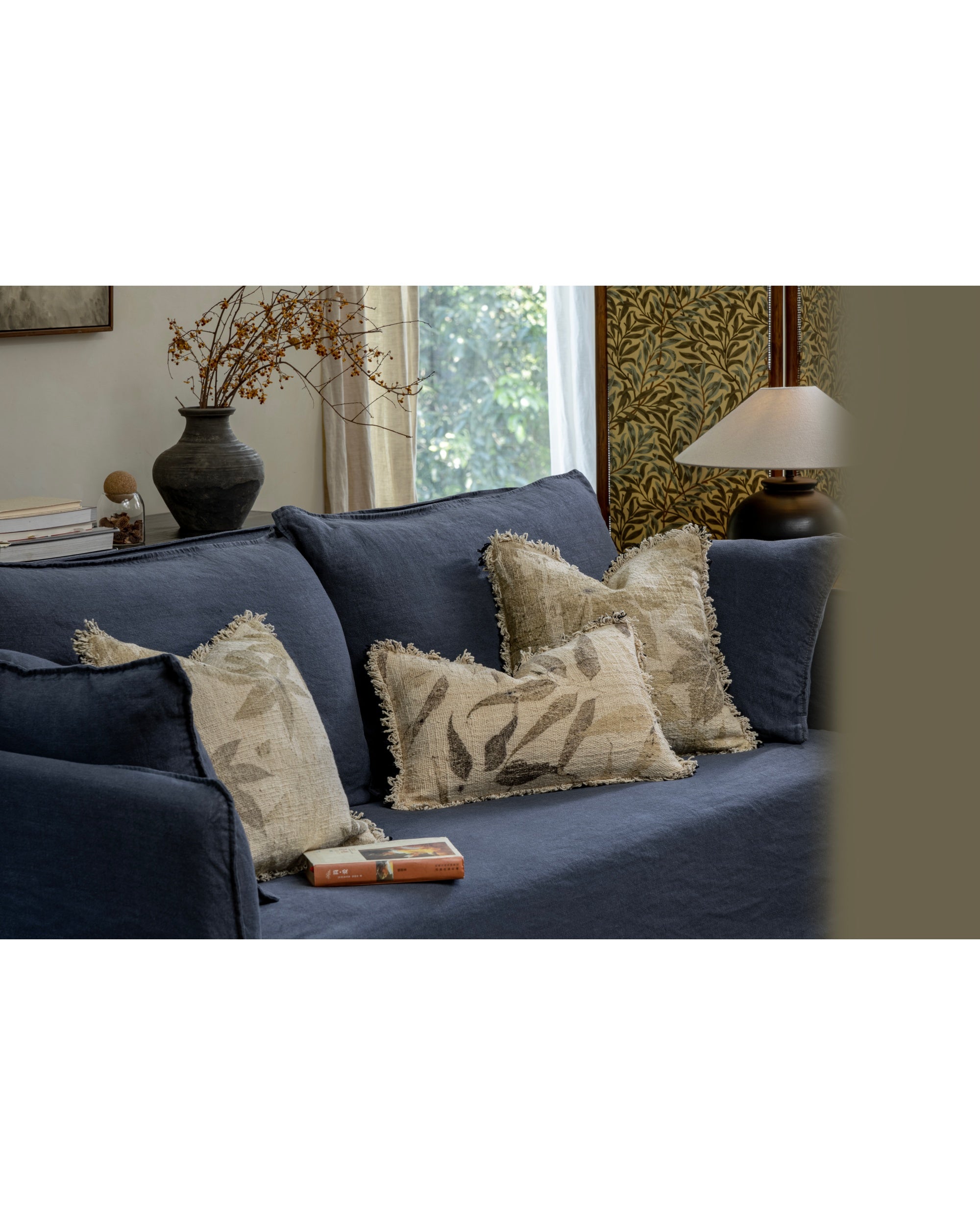 Verda Pillow: Cotton accent pillow with botanical print and fringe on navy sofa.