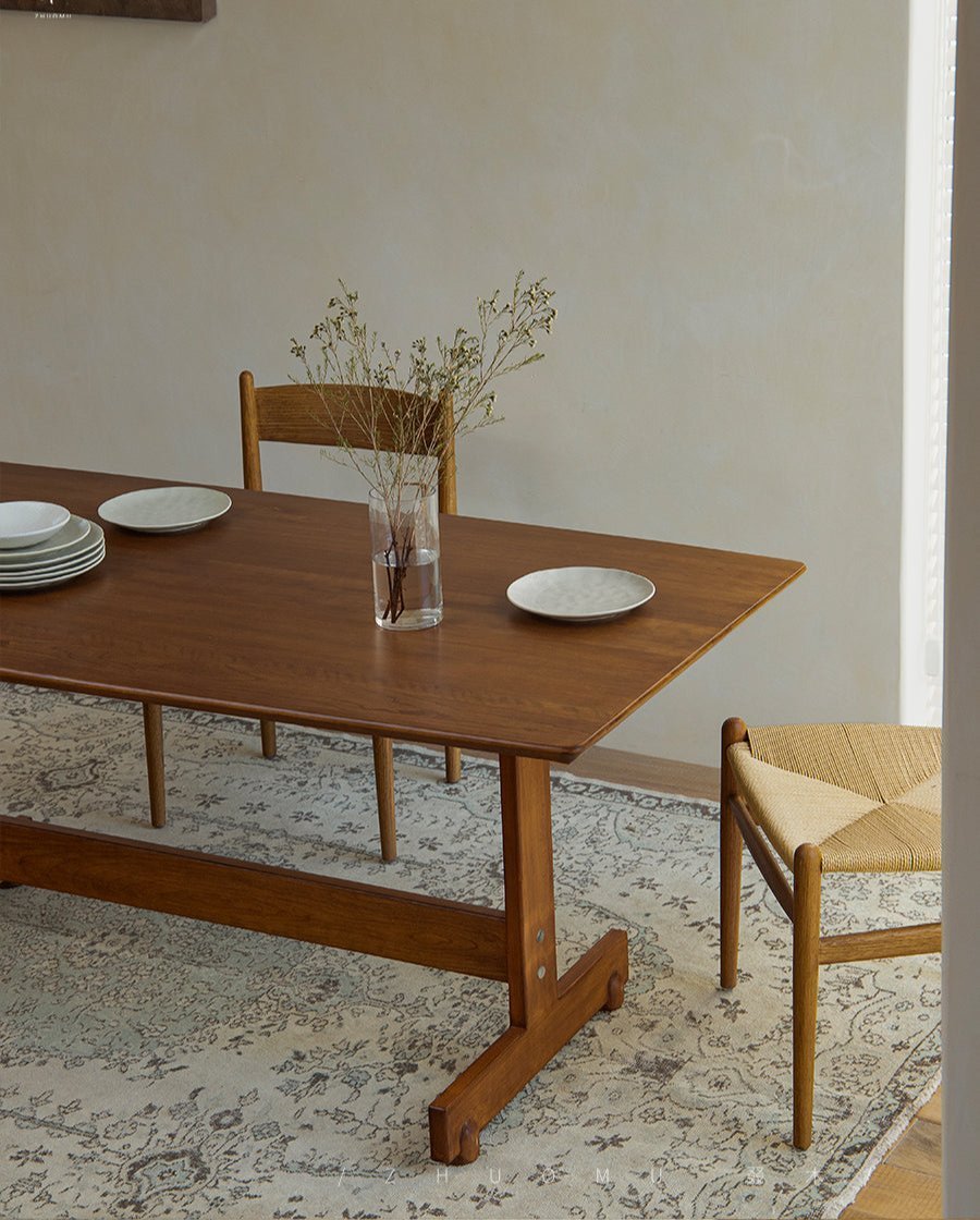 Hoof Dining Table solid wood with I-shaped base, set in a cozy dining setting with plates and chairs on rug