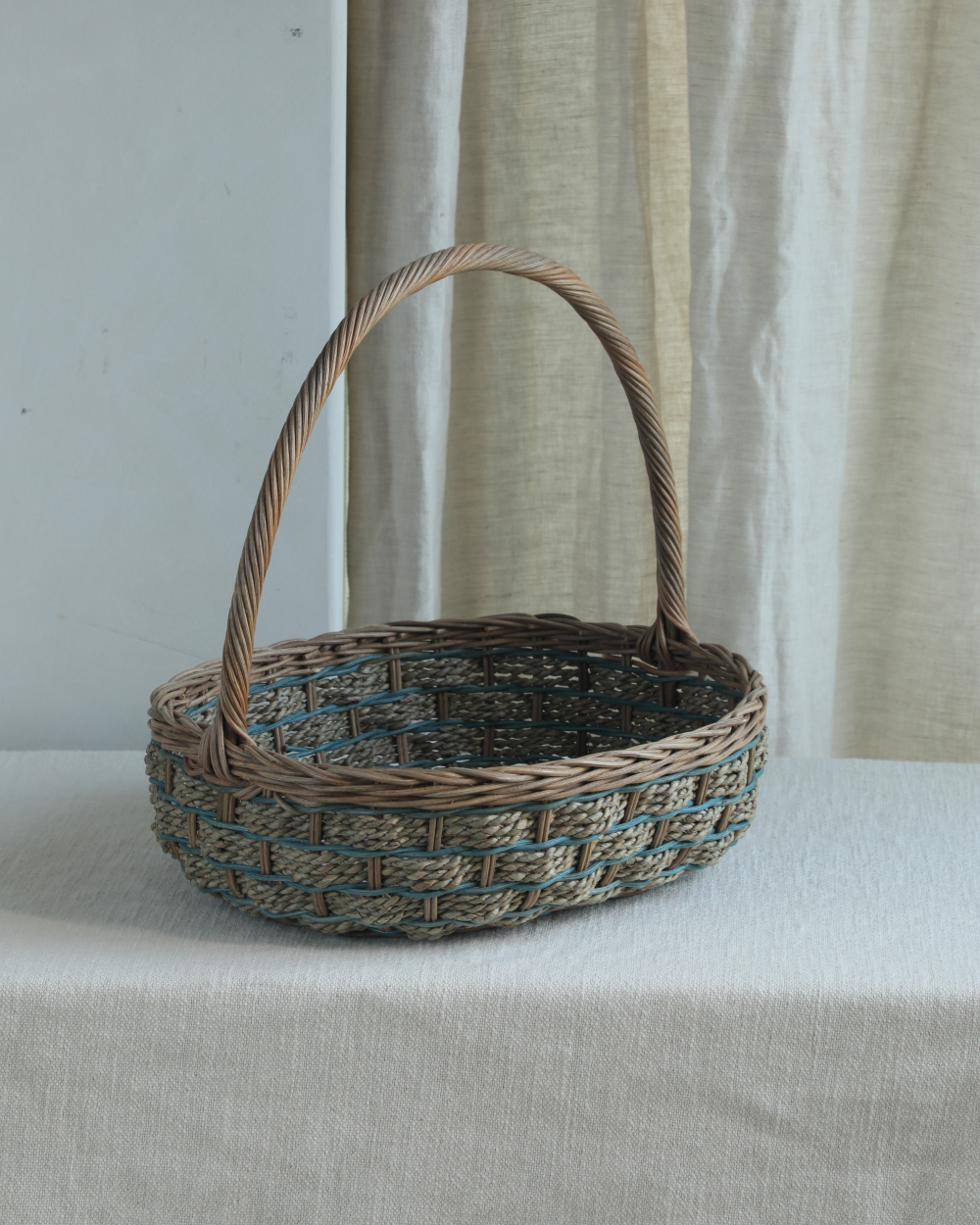 Viney Tote Basket: Oval woven rattan with blue accents and twisted handle.