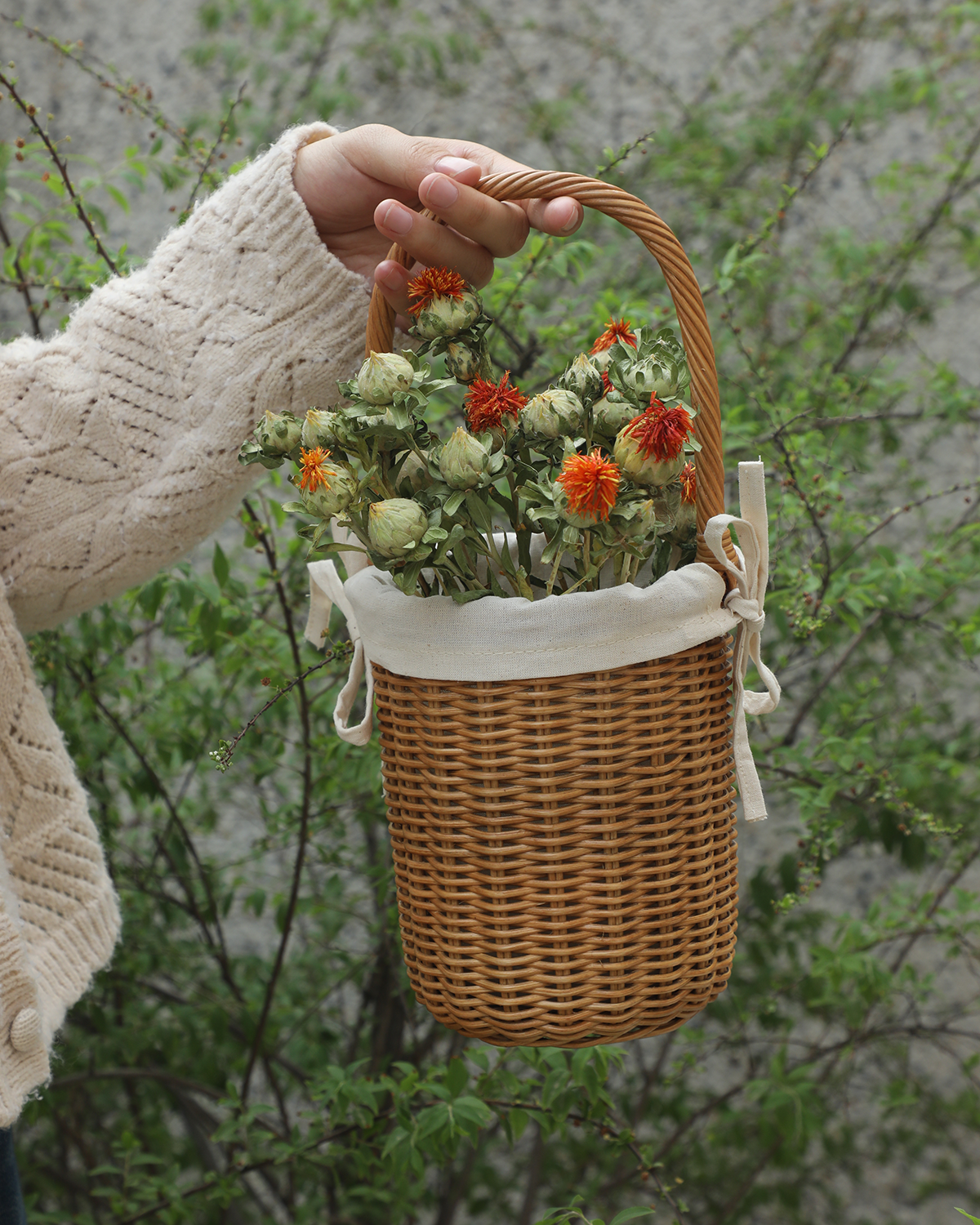 Hand holding natural woven rattan Iris basket with cotton lining, filled with dried flowers.