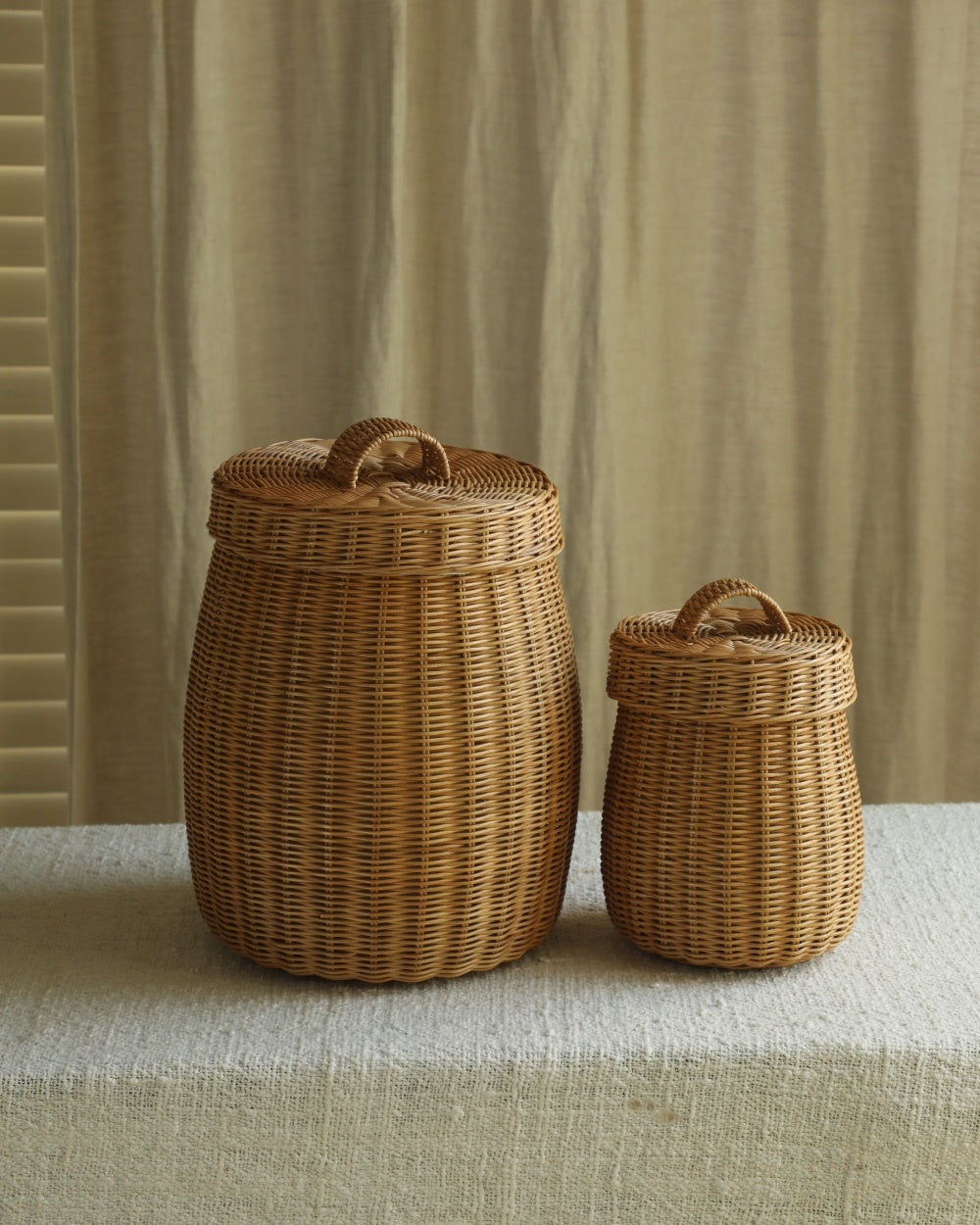 Two Elodie round storage baskets in natural woven rattan, with lids and handles.