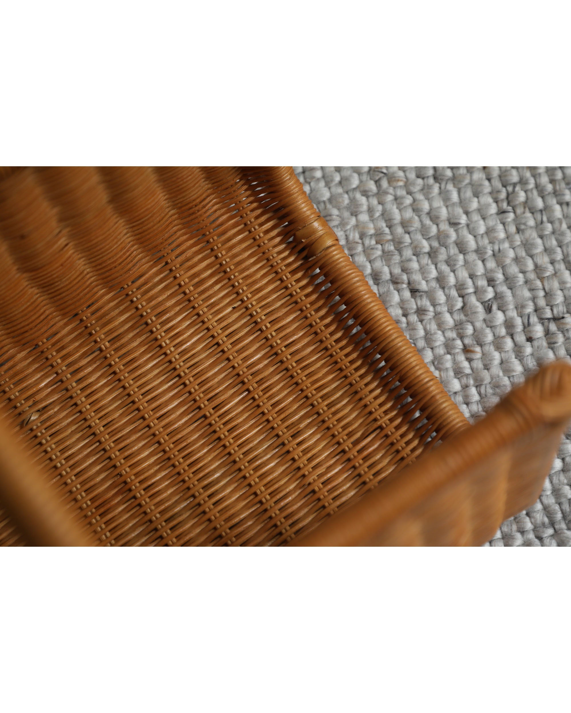 Close-up of the textured wicker weave of the brown Folio Caddy basket, placed on a grey rug.