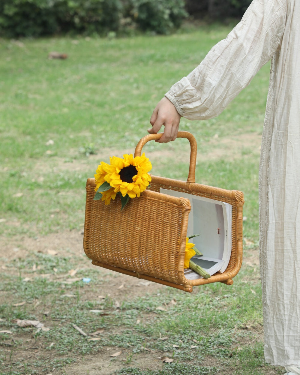Person holding woven Folio Caddy book basket with integrated handle and sunflowers.