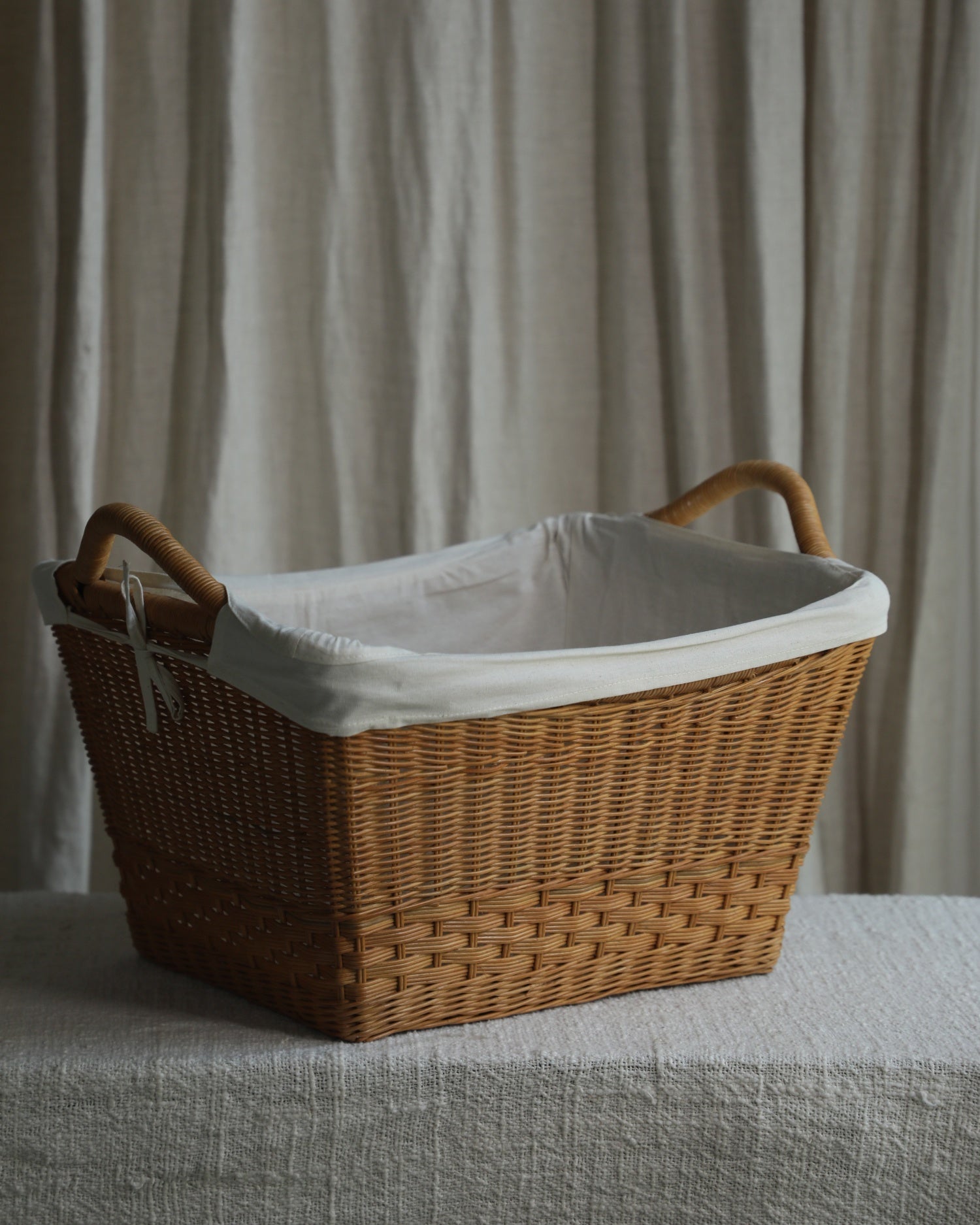 Large handwoven rattan storage basket with cotton lining and double handles.