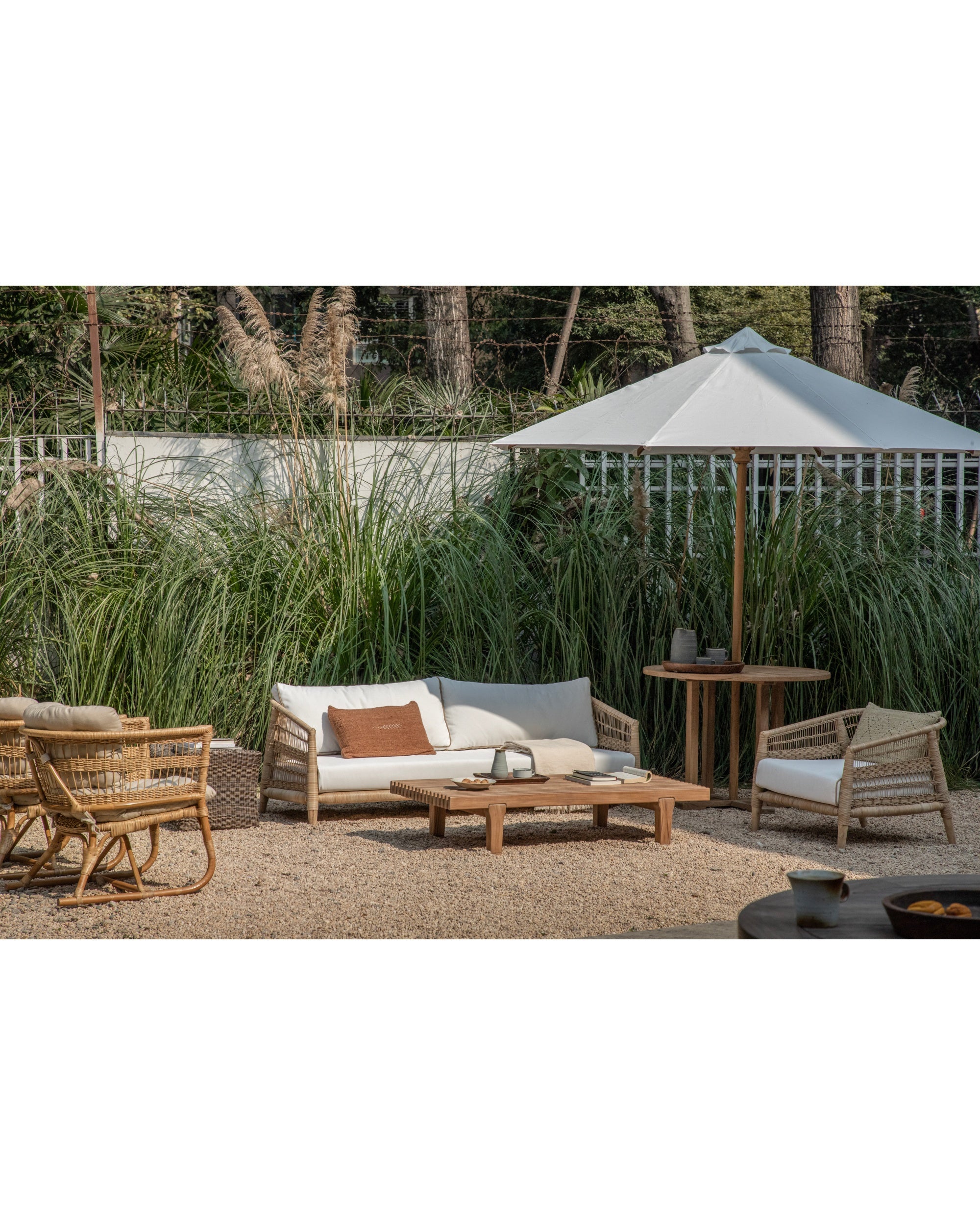 Durable teak patio table & rattan seating set with spacious white umbrella.