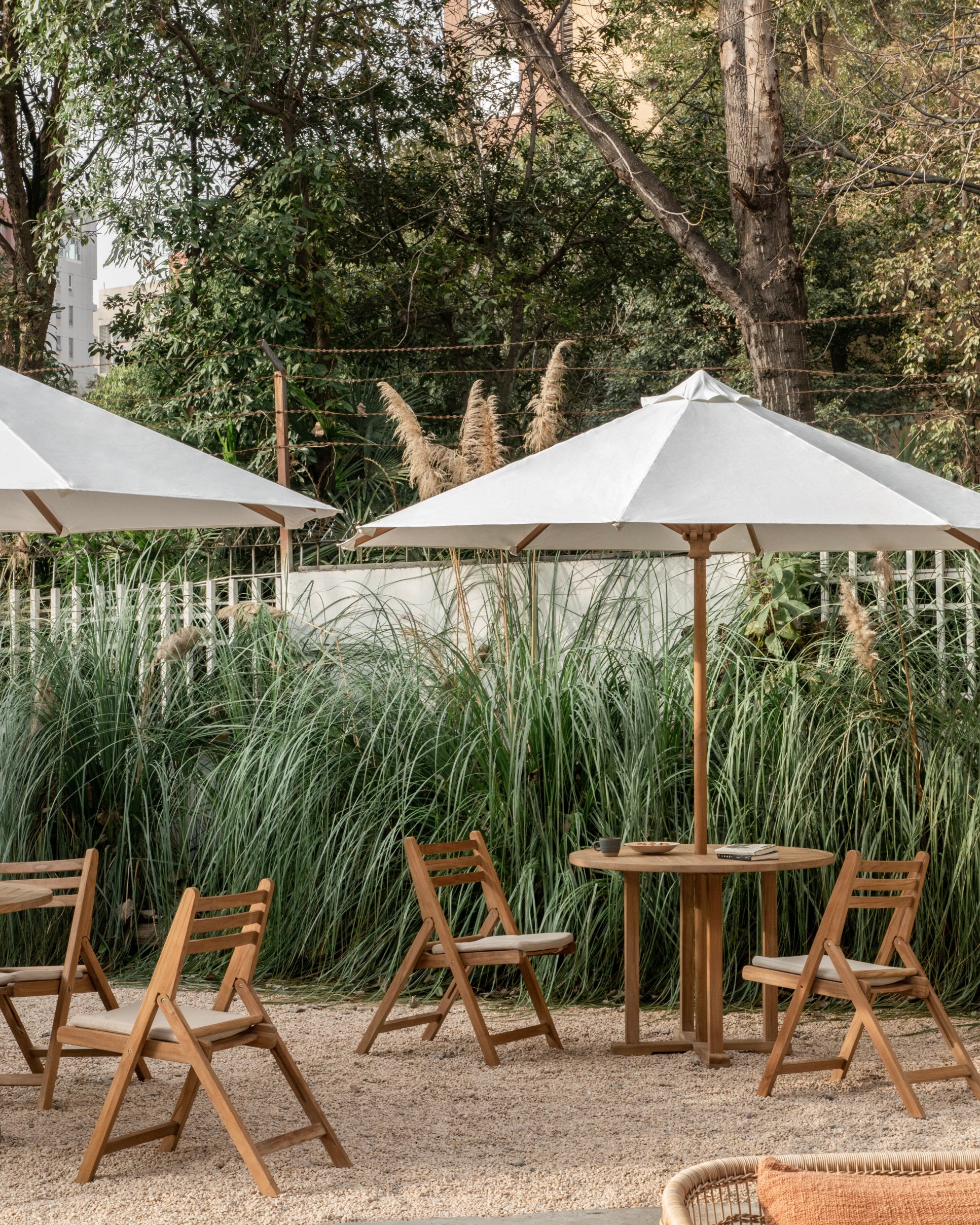 Outdoor seating area with wooden tables and chairs under large white umbrellas, surrounded by greenery.